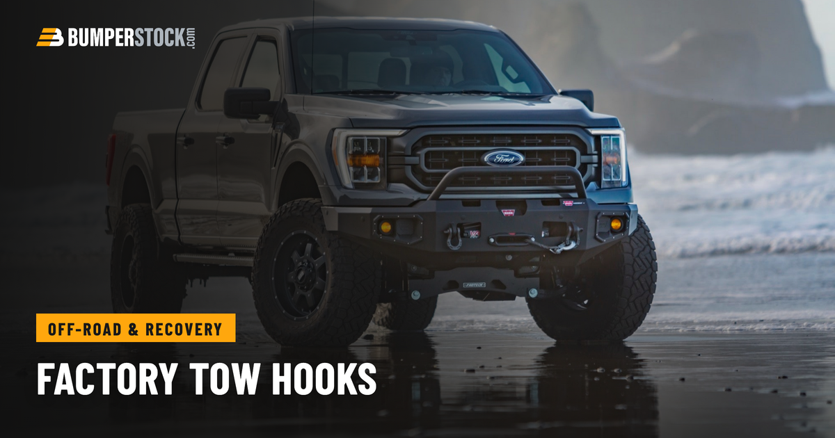 A Ford F150 on wet sand wearing a Warn Ascent front winch bumper with shackle mounts built into the bumper face.