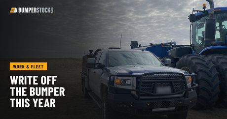 A customer's GMC Sierra 2500HD farm truck with a Ranch Hand Midnight steel front bumper, parked beside a tractor in a harvested field